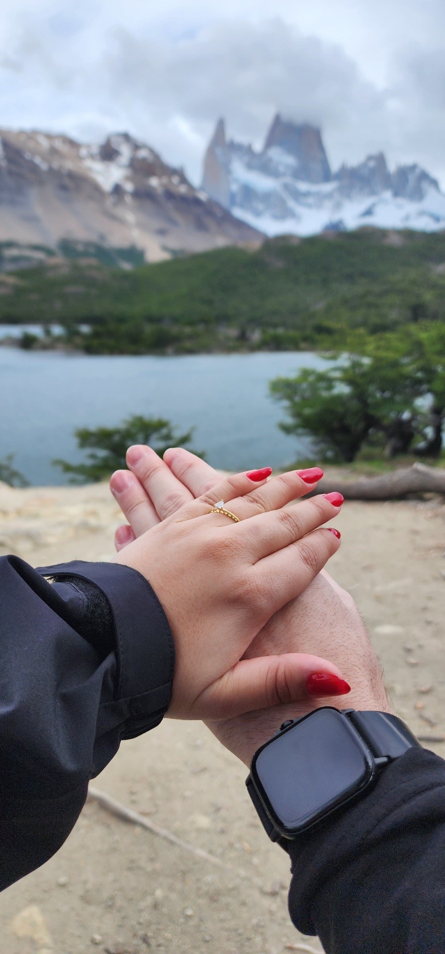 Mãos entrelaçadas com o anel de noivado, montanhas ao fundo